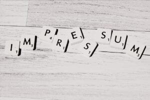 Symbolbild: Scrannle-Spielsteine bilden das Wort "Impressum" auf einem hellgrauen Holzboden